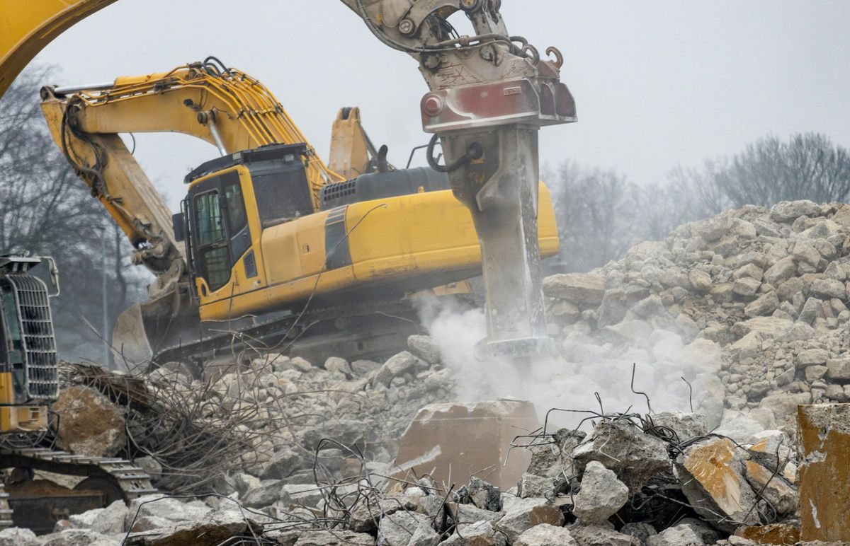 Graafmachine met sloophamer breekt betonblokken op een berg puin