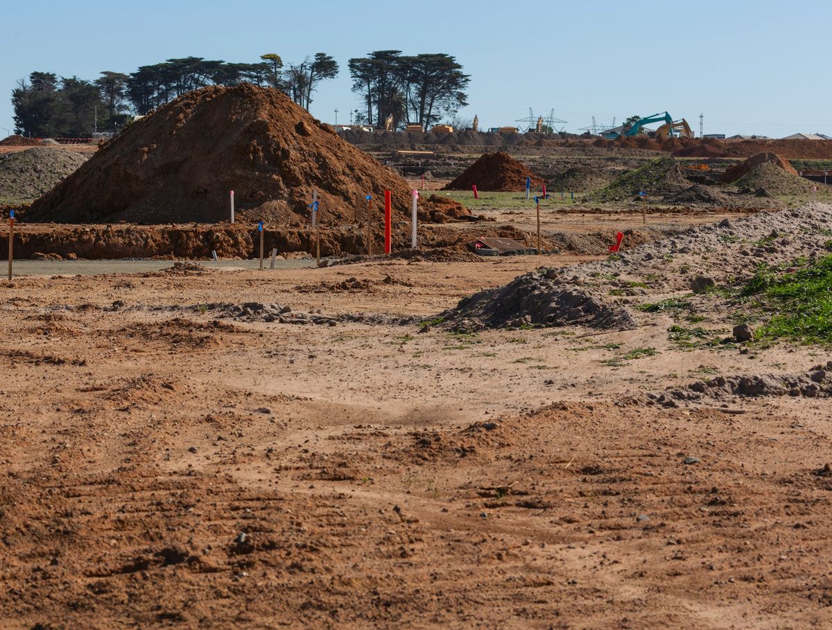 Geruimd en geëgaliseerd bouwterrein met uitzetpaaltjes en een hoop aarde