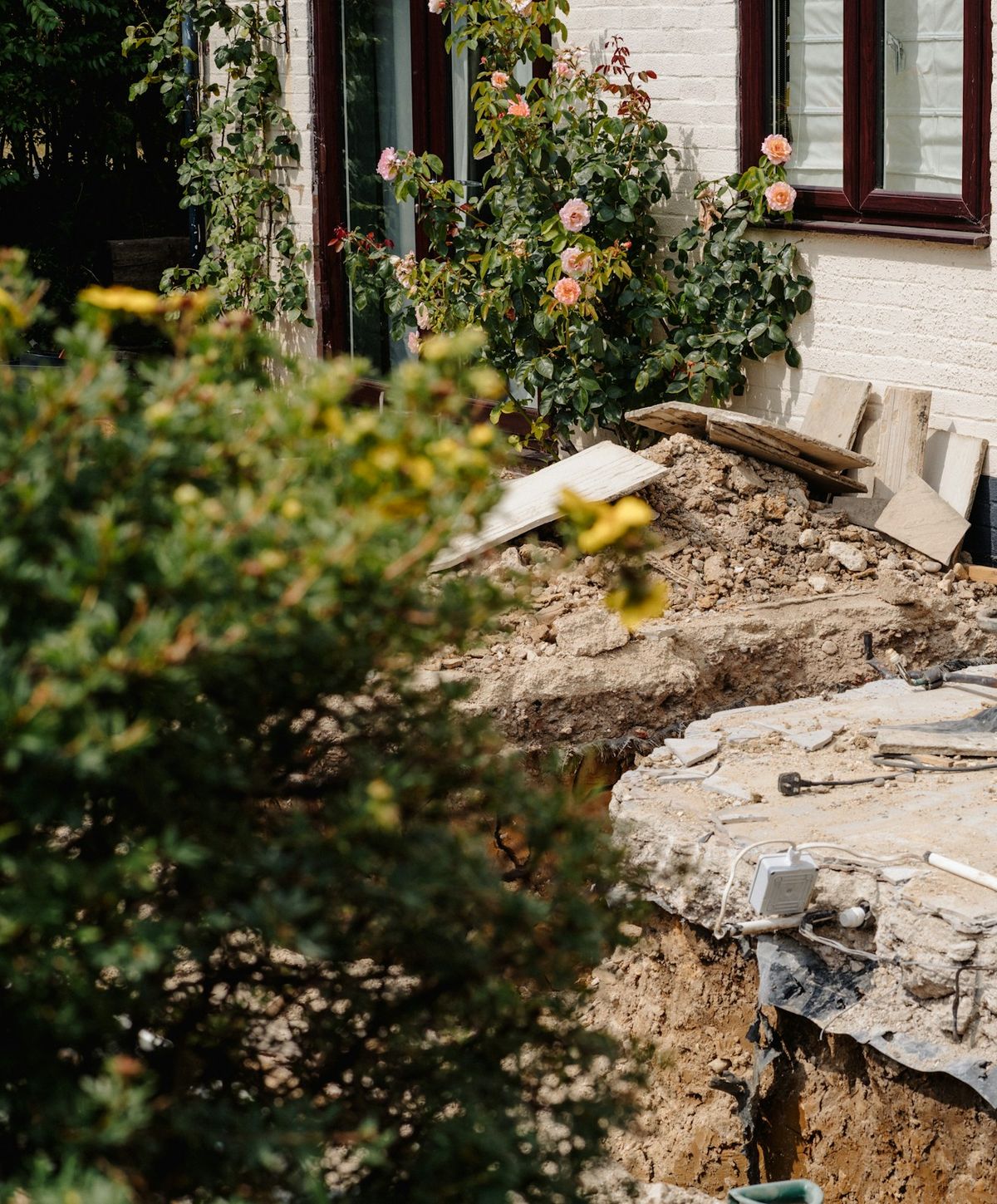 Opgebroken grond en puin naast een woning met rozen tegen de gevel